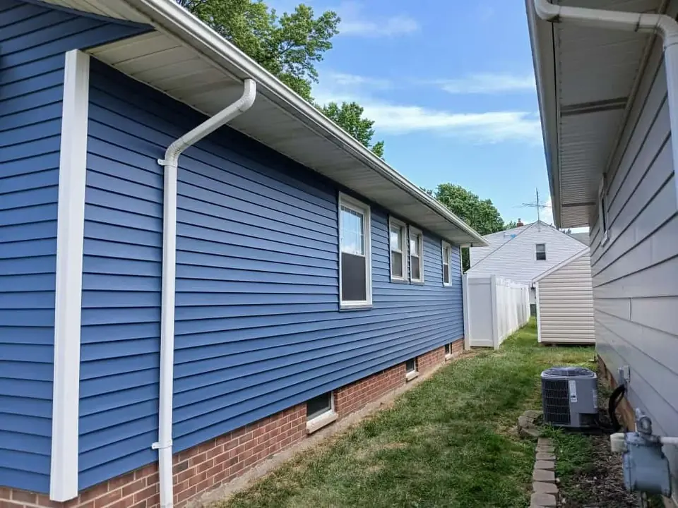 Blue vinyl siding along a single-story home with white gutters and a downspout.