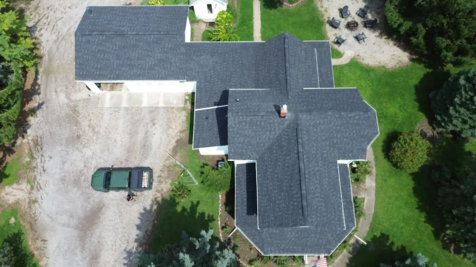 Overhead aerial view of a completed dark shingle roof on a farmhouse and its outbuildings.